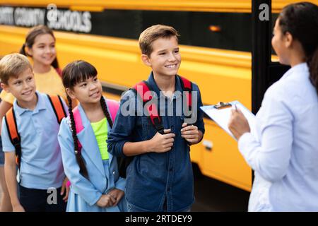 Glückliche Schulkinder warten darauf, in den Schulbus zu steigen, und stehen abwechselnd Stockfoto