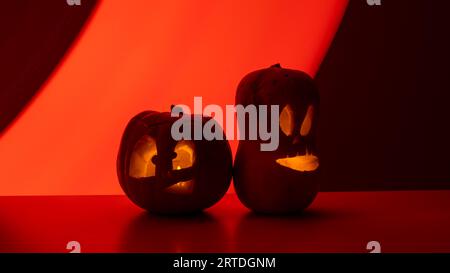 Zwei Jack-o-Laternen leuchten im Dunkeln auf rotem Hintergrund. Halloween Dekoration. Stockfoto