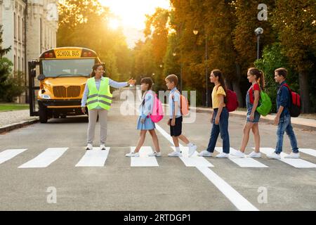 Sicherheit Im Straßenverkehr. Schulbusassistent Hilft Kindern, Die Straße Mit Dem Crosswalk Zu Überqueren Stockfoto