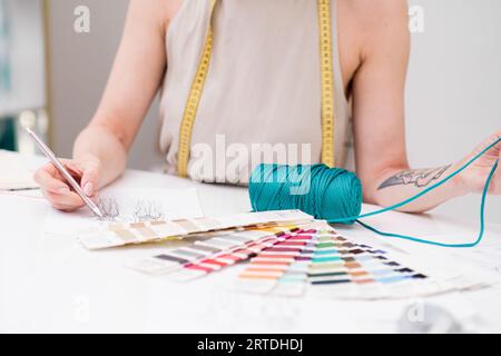 Die Schneiderin zeichnet Kleidung mit grünem Garn am Arbeitsplatz in einem Modeatelier Stockfoto