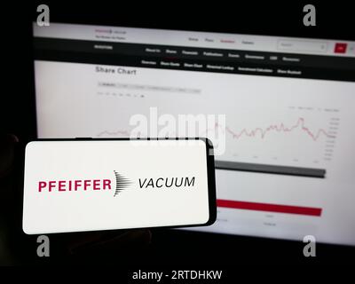 Person, die ein Mobiltelefon mit dem Logo der Pfeiffer Vacuum Technology AG auf dem Bildschirm vor der Webseite hält. Konzentrieren Sie sich auf das Display des Telefons. Stockfoto