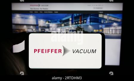 Person, die ein Mobiltelefon mit dem Logo der Pfeiffer Vacuum Technology AG auf dem Bildschirm vor der Webseite hält. Konzentrieren Sie sich auf das Display des Telefons. Stockfoto