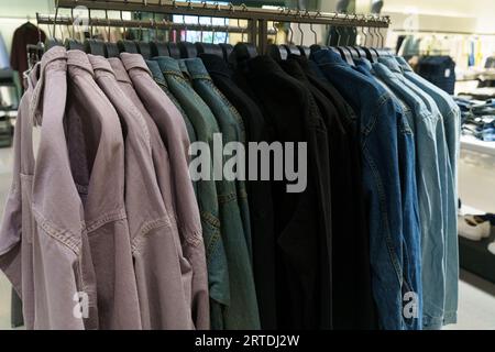 Denimhemden mit langen Ärmeln hängen in einem Bekleidungsgeschäft auf Kleiderbügeln. Nahaufnahme, Hintergrund. Stockfoto