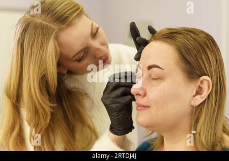 Porträt einer Frau, die in einem Schönheitssalon ihre Augenbrauen mit einer Pinzette zupfen lässt. Schönheitsindustrie. Stockfoto