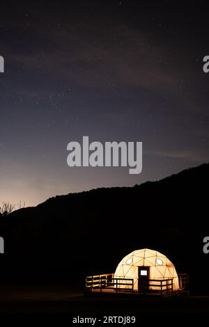Eine geodätische Kuppel leuchtet unter dem Nachthimmel in den rauchigen Bergen Stockfoto