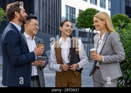 Eine Gruppe verschiedener Geschäftsleute, männlicher und weiblicher Kollegen, die gemeinsam in einer Mittagspause außerhalb des Büros ein lustiges und freundliches Gespräch führen und Tassen Kaffee halten, vier-Personen-Team. Stockfoto