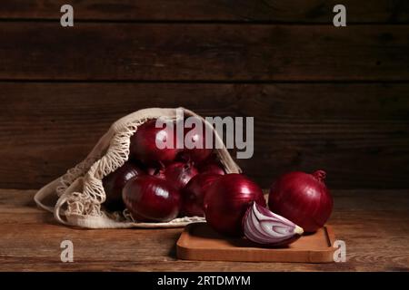 Brett und Fadenbeutel mit frischen roten Zwiebeln auf hölzernem Hintergrund Stockfoto