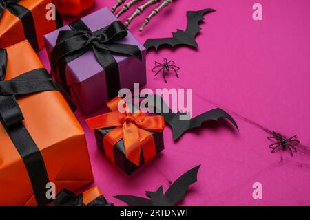 Komposition mit Geschenkboxen, Spinnen und Papierschlägern für Halloween auf lila Hintergrund, Nahaufnahme Stockfoto