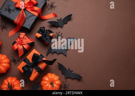 Komposition mit Geschenkboxen, Kürbissen, Spinnen und Papierschlägern für Halloween auf braunem Hintergrund Stockfoto