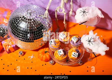 Halloween-Party-Komposition mit Cupcakes, Disco-Ball, Getränk und Deko auf orangefarbenem Tisch Stockfoto