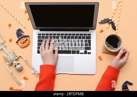 Weibliche Hände mit Laptop-, Kaffee- und Halloween-Deko auf beigem Hintergrund Stockfoto