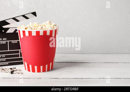 Popcorn-Eimer mit Filmklapperbrett und Halloween-Strohhalmen auf Holztisch vor weißem Hintergrund Stockfoto