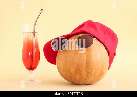 Halloween Kürbis mit Strandaccessoires und einem Glas leckeren Cocktails auf beigem Hintergrund Stockfoto