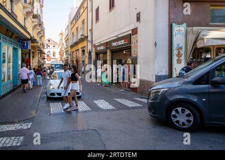 Die schmale Via Luigi de Maio Straße, die nur auf einer Seite einen Bürgersteig hat. Die Überquerung führt zur Via S Cesareo, einer engen Gasse voller Touristenläden im Herzen von Sorrent. Sorrento ist eine Küstenstadt im Südwesten Italiens mit Blick auf die Bucht von Neapel auf der sorrentinischen Halbinsel. Hoch oben auf Klippen, die die Stadt von ihren geschäftigen Yachthäfen trennen, ist sie bekannt für ihren atemberaubenden Blick auf das Wasser und die Piazza Tasso, ein von Cafés gesäumter Platz. Stockfoto