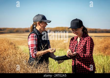 Eine Landwirtin, die auf den Feldern steht und ihren Lehrling gerne über moderne Anbautechniken für Rapskulturen mit drahtlosen Technologien unterrichtet... Stockfoto