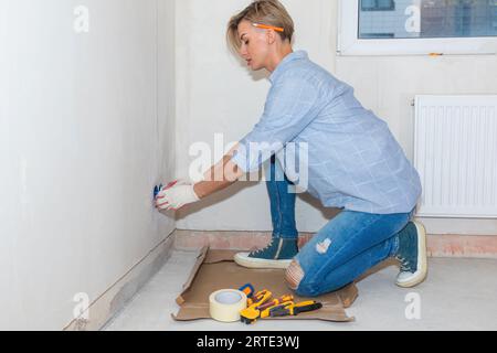 Eine Elektrikerin installiert Steckdosen in der Zimmerwand. Renovierung in neuem Apartment. Hausreparatur. Hochwertiges Foto Stockfoto