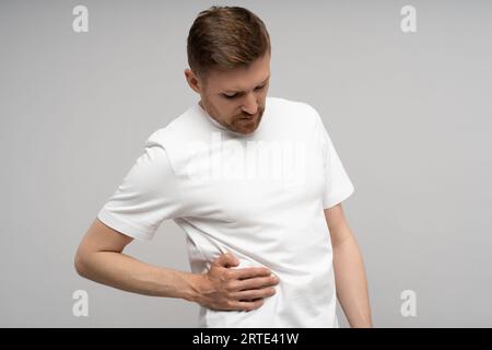 Mann, der Schmerzen im rechten Teil des Abdomens spürt, an Spasmen auf grauem Hintergrund leidet. Stockfoto
