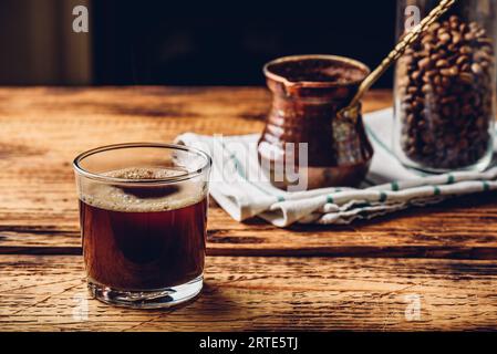 Frisch gebrühter türkischer Kaffee im Trinkglas. Cezve und Glas gerösteten Kaffeebohnen. Stockfoto