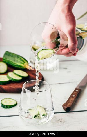 Hand mit Kanne gießt Wasser mit geschnittener Gurke Stockfoto