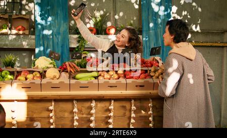 Lokaler Anbieter und Kunde, der Fotos mit dem Smartphone am Stand des Bauernmarktes macht, Kunden besucht und kleine Unternehmen im Internet fördert. Machen Sie gemeinsam Fotos auf Messe. Stockfoto