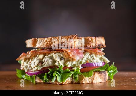 Avocado-Eiersalat-Sandwich mit Speck, Salat, Tomaten und roten Zwiebeln Stockfoto