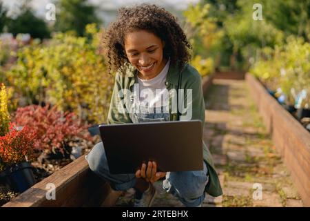 Gärtnerin, die am Laptop arbeitet, während sie auf dem Hintergrund des Shopplants Centers sitzt Stockfoto