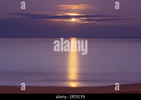 Goldenes Licht reflektiert auf dem Pazifischen Ozean mit dem Vollmonduntergang im Kamaole Beach Park; Kihei, Maui, Hawaii, Vereinigte Staaten von Amerika Stockfoto