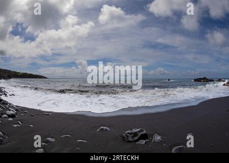 Scenic view of the Pacific Ocean from a black lava sand beach with sea surf and blue, cloudy sky along the Road to Hana, scenic route Stock Photo