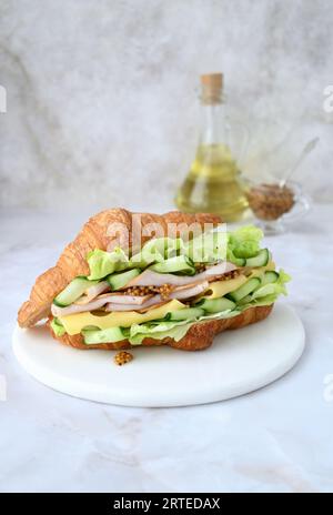 Croissant mit Schinken, Maasdam-Käse, Salat, Gurke und Dijon-Senf Stockfoto