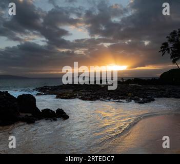 Sonnenstrahlen durch die Wolken und reflektieren auf dem Wasser am Secret Beach mit Blick auf die Bucht und den Pazifischen Ozean in der Dämmerung mit Silhouette... Stockfoto