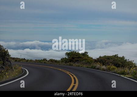 Nahaufnahme einer scharfen Kurve auf dem asphaltierten Highway mit Blick von oben über den Wolken auf dem Berghang auf der Straße von Haleakala Stockfoto