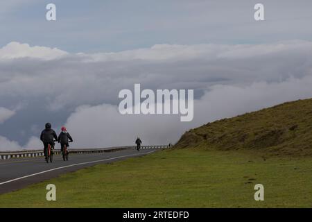 Blick von hinten auf Menschen, die auf der asphaltierten Straße von Haleakala abwärts fahren, und genießen Sie die dramatische Aussicht auf die Wolken über der Pazifikküste Stockfoto