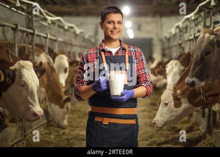 Ein Landwirt hält ein Glas Milch und lächelt auf einem Milchviehbetrieb mit Kühen Stockfoto