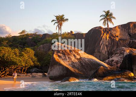 Frau, die am berühmten Strand der Bäder gegen die großen vulkanischen Felsformationen in den BVI's in der Dämmerung spaziert Stockfoto