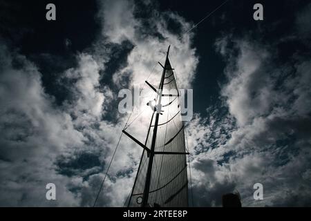 Silhouette eines Mannes, der einen Segelmast vor einem blauen, bewölkten Himmel mit Sonnenaufgang beim Mt Gay Rum Yacht Race klettert, das die Insel umrundet... Stockfoto