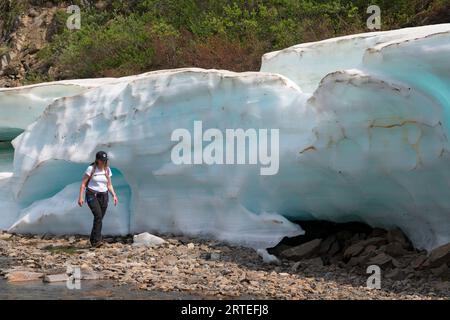 Frau, die herumläuft und die Eisformation der späten Saison erforscht, die als aufeis bekannt ist (entsteht durch mehrere Wasserschichten, die übereinander gefrieren... Stockfoto