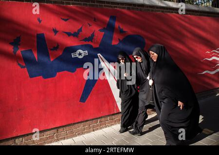 Teheran, Iran. September 2023. Drei iranische Frauen in schwarzen Chadoren laufen an einem Wandgemälde entlang der Wand der ehemaligen US-Botschaft vorbei. Ein Jahr nachdem der Tod von Mahsa Amini Unruhen im ganzen Iran auslöste, bleibt das Thema Hijab ein schmerzhafter Ort. Doch eine verkrüppelte Wirtschaftskrise hat viele mit dem Ende beschäftigt. (Bild: © Rouzbeh Fouladi/ZUMA Press Wire) NUR REDAKTIONELLE VERWENDUNG! Nicht für kommerzielle ZWECKE! Stockfoto