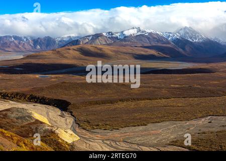 Blick auf schneebedeckte Berge und herbstfarbenes Tundra-Tal und Toklat River vom Polychrome Pass an einem sonnigen, bewölkten Tag im Herbst, Denali Na... Stockfoto