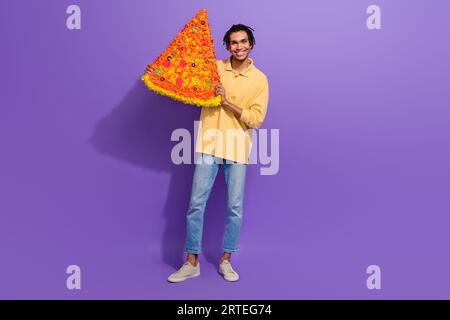 Ganzkörpergröße Foto von freundlichen Mann Student bestellen billige Pizza Lieferung Scheibe italienische riesige Mahlzeit Essen isoliert auf violetter Farbe Hintergrund Stockfoto