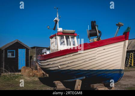 Rotes, weißes und blaues Fischerboot, das im Sonnenlicht an der Küste angedockt wird; Southwold, Suffolk, England Stockfoto
