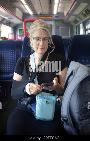 Reife Frau fährt mit öffentlichen Verkehrsmitteln und benutzt ihr Smartphone Stockfoto