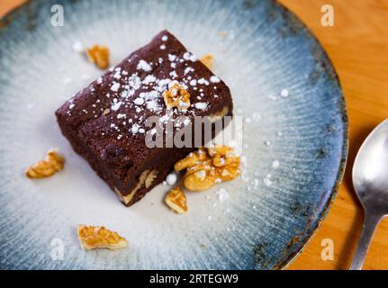 Ein Stück Schokoladen-Nuss-Kuchen wird auf einem Teller serviert, der um den Rand mit Stücken Walnüsse verziert ist Stockfoto