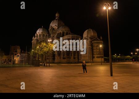 Frau steht und bewundert die Kathedrale von Marseille bei Nacht, mit einer hellen Straßenlaterne im Dunkeln; Marseille, Frankreich Stockfoto