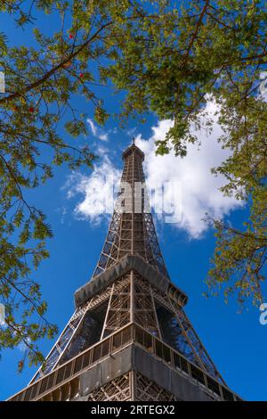 Flacher Blick auf den Eiffelturm vor blauem Himmel mit Wolken, umgeben von Ästen; Paris, Frankreich Stockfoto