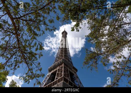 Flacher Blick auf den Eiffelturm vor blauem Himmel mit Wolken, umgeben von Ästen; Paris, Frankreich Stockfoto