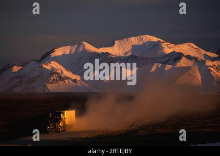 Der Transport Truck fährt entlang des Dalton Highway mit schneebedeckten Bergen im Hintergrund; Alaska, Vereinigte Staaten von Amerika Stockfoto