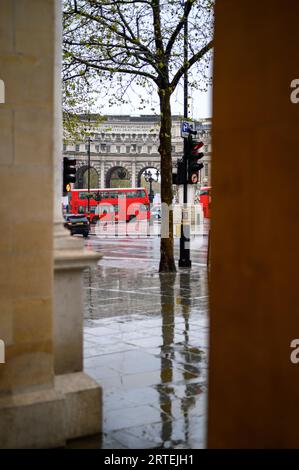 LONDON - 24. April 2023: Der legendäre rote Londoner Bus verleiht dem regnerischen Tag am Admiralty Arch Lebendigkeit. Stockfoto