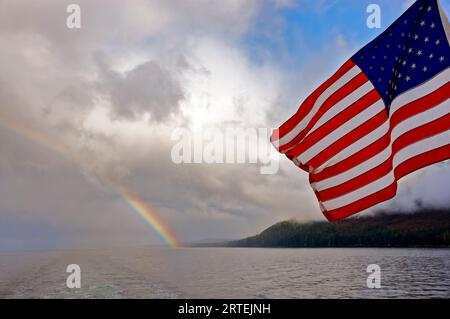Regenbogen und eine amerikanische Flagge flattern vom Heck eines Bootes, in der Nähe von Petersburg, Alaska, USA; Alaska, Vereinigte Staaten von Amerika Stockfoto