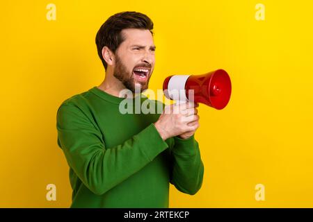 Foto eines jungen lustigen Geschäftsmannes trägt grünen Pullover schreienden Megaphon Aggression Rede Konflikt isoliert auf gelbem Hintergrund Stockfoto