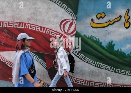 Teheran, Iran. September 2023. Zwei iranische Frauen laufen an einem Wandgemälde der iranischen Flagge in der Innenstadt von Teheran vorbei. Ein Jahr nachdem der Tod von Mahsa Amini Unruhen im ganzen Iran auslöste, bleibt das Thema Hijab ein schmerzhafter Ort. Doch eine verkrüppelte Wirtschaftskrise hat viele mit dem Ende beschäftigt. (Bild: © Rouzbeh Fouladi/ZUMA Press Wire) NUR REDAKTIONELLE VERWENDUNG! Nicht für kommerzielle ZWECKE! Stockfoto